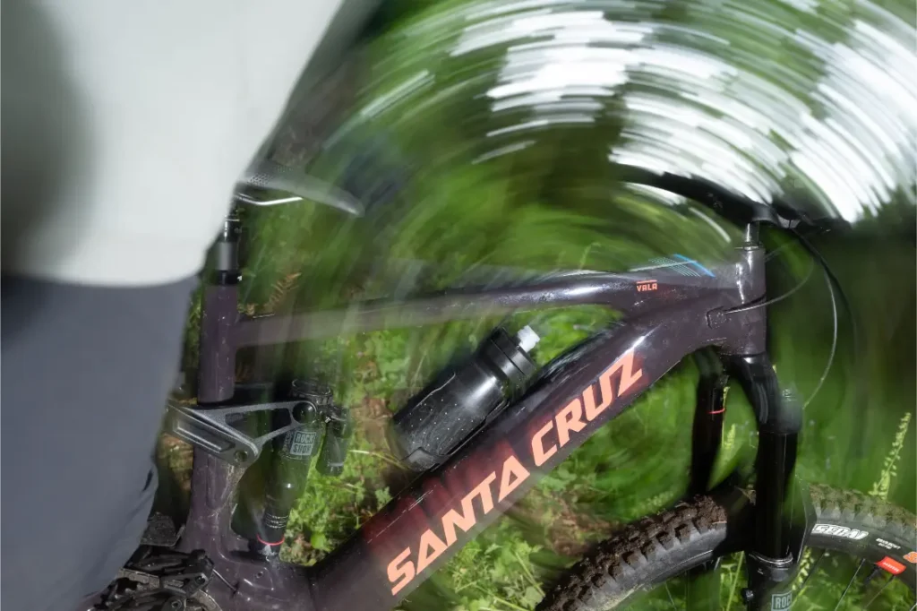 Una bicicleta de aluminio Santa Cruz Vala AL con una botella de agua montada en el cuadro, fotografiada con un efecto de desenfoque de movimiento arremolinado.