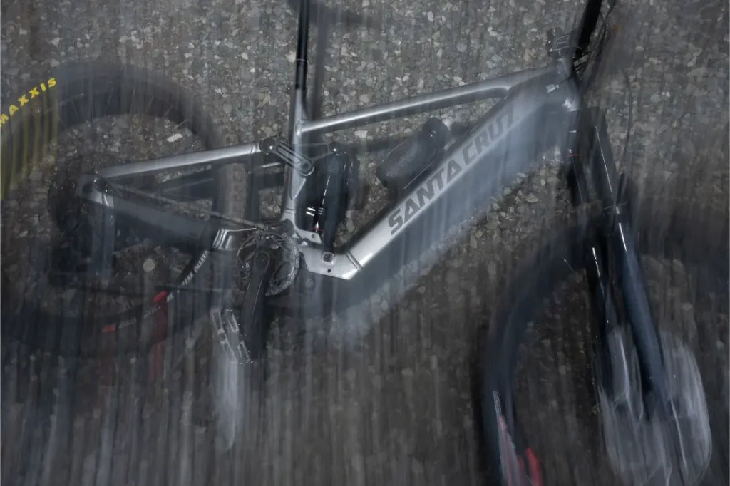 Una bicicleta de montaña Santa Cruz Vala AL, fabricada en robusto aluminio, descansa sobre la grava, parcialmente difuminada por las rayas del agua o el movimiento.