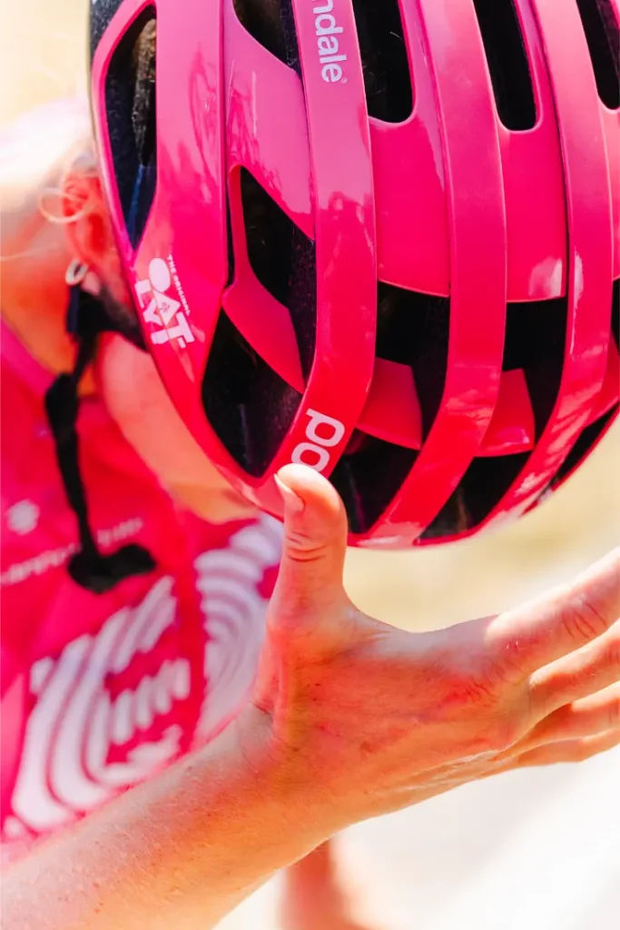 Un ciclista ataviado con un casco ventilado de color rosa chillón y un maillot a juego se seca el sudor de la frente con la mano durante un paseo.