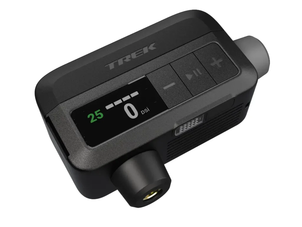 Un manómetro digital compacto, perfecto para el inflado de ruedas, con una pantalla que muestra "25" y "0 psi", botones etiquetados y el nombre de la marca "TREK" en la parte superior, compatible con la bomba eléctrica Trek Air Rush.