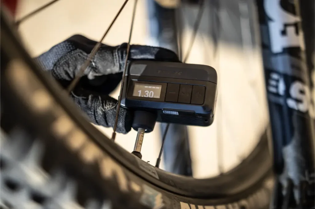 Una mano enguantada utiliza un manómetro digital Trek Air Rush para medir la presión de aire de un neumático de bicicleta, mostrando 1,30 en la pantalla.
