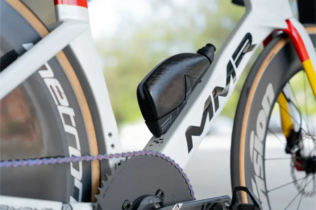 Primer plano de un cuadro de bicicleta MMR blanco con una botella de agua negra montada cerca del plato, mostrando parte de la cadena, la biela y la rueda, como las que Las cadenas KMC impulsan al Caja Rural-Seguros RGA.