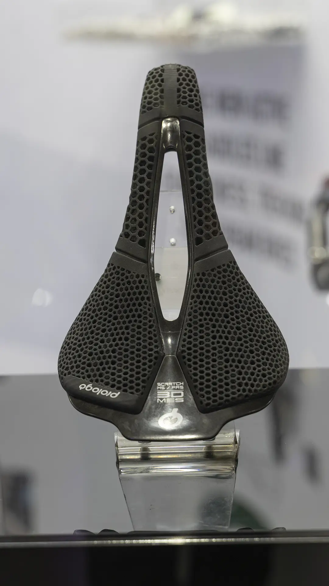 Un sillín de bicicleta ergonómico Prologo Scratch M5 PAS 3DMSS negro con un patrón de panal de abeja se muestra en posición vertical sobre una superficie reflectante.