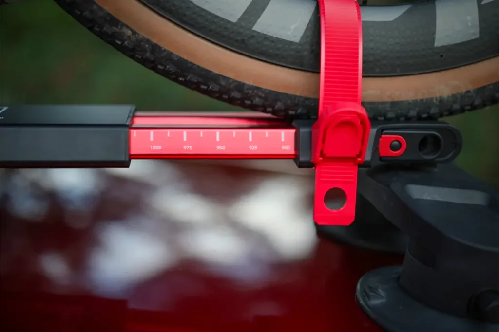 Primer plano de una rueda de bicicleta sujeta con una correa roja a un portabicicletas Allen Smart Suction, con una escala roja de medición en milímetros en el portabicicletas montado en el techo.