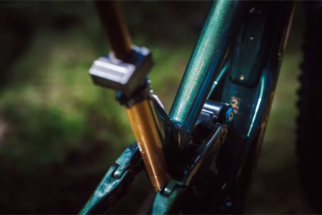 Primer plano del cuadro y la suspensión trasera de una bicicleta, destacando la pintura verde metalizada y el amortiguador dorado de la FOX 38 Racing Green Edición Limitada.