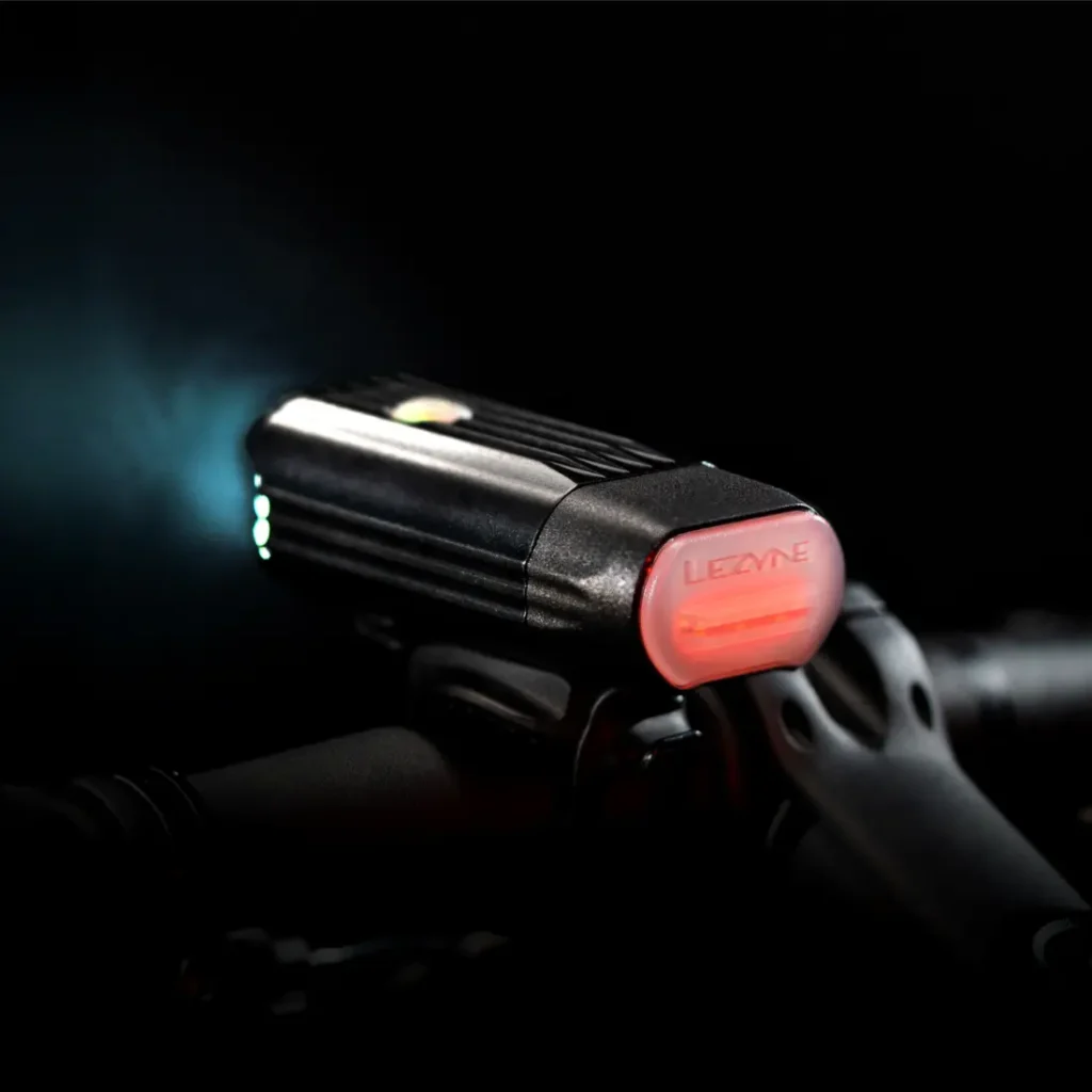 Primer plano de una luz de bicicleta Lezyne con el sistema Lezyne Radar React montado en el manillar, la luz blanca delantera encendida y una luz roja trasera visible.