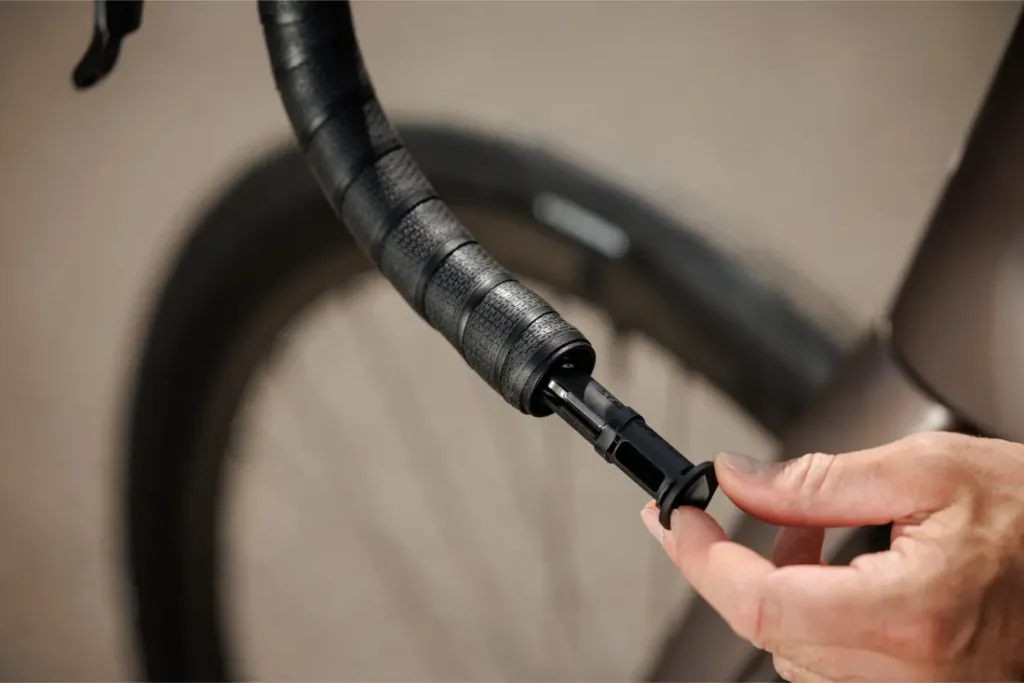 Una mano inserta un tapón de extremo de manillar en el manillar de una bicicleta SCOTT Addict envuelta en cinta negra.