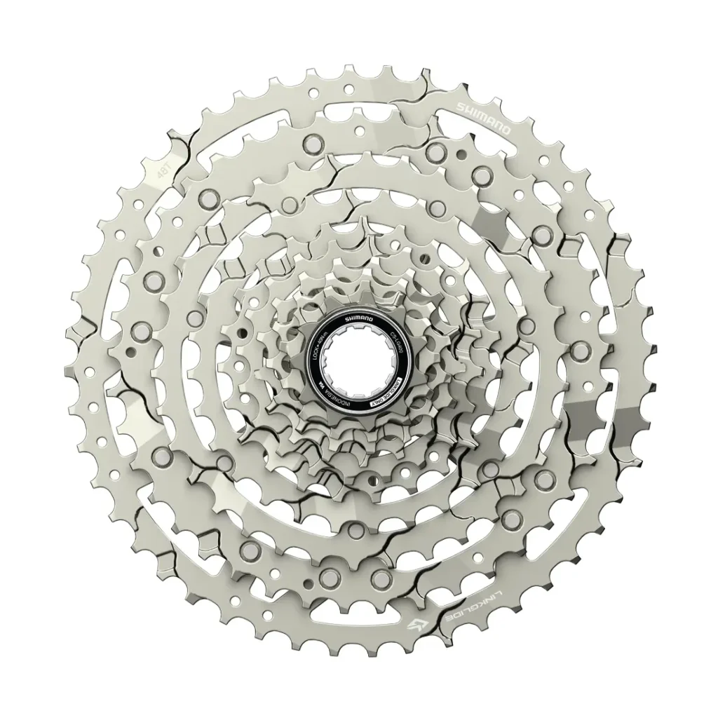 Un casete de bicicleta plateado Edición Aluminio Pulido con múltiples piñones dispuestos en un patrón circular, visto desde arriba, perfecto para mejorar su Shimano CUES u otras configuraciones de grupos de carretera.