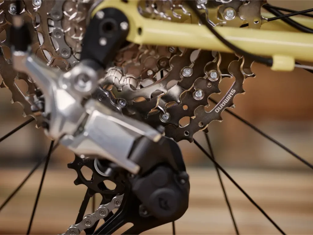Primer plano del cambio trasero y el casete de una bicicleta, destacando los cambios Shimano CUES y la cadena, con especial atención a los componentes mecánicos fabricados en Aluminio Pulido.