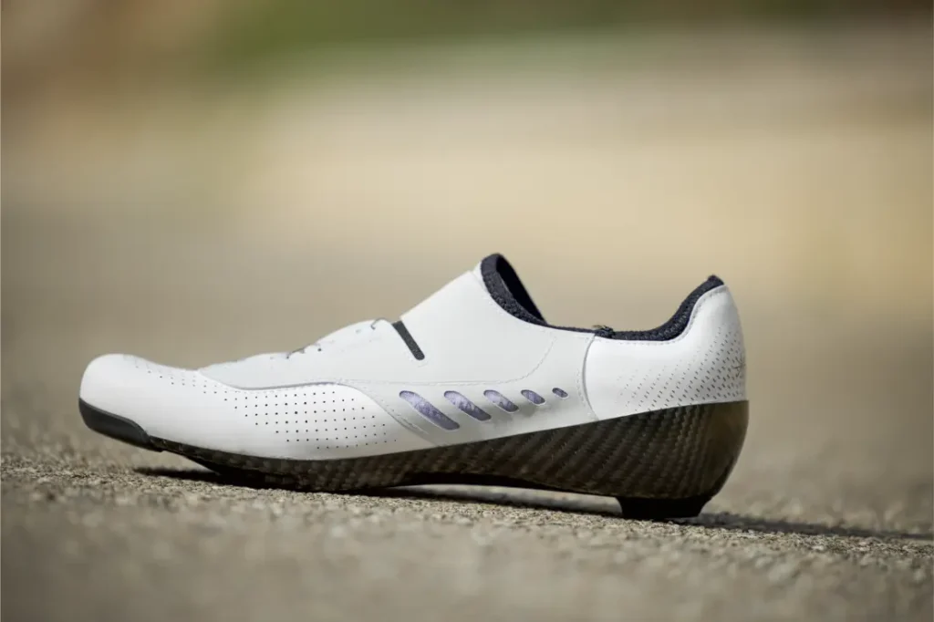 Unas Zapatillas Q36.5 Unique Pro blancas de corte bajo para ciclismo con detalles en negro y suela de fibra de carbono descansan sobre una superficie pavimentada, diseñada para obtener el máximo rendimiento.