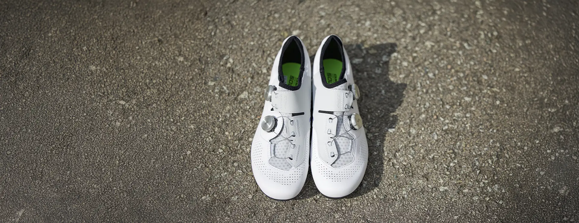 Un par de zapatillas de ciclismo Q36.5 Unique Pro con interiores negros y plantillas verdes se colocan una al lado de la otra sobre hormigón rugoso, reflejando un rendimiento de primer nivel para ciclistas dedicados.