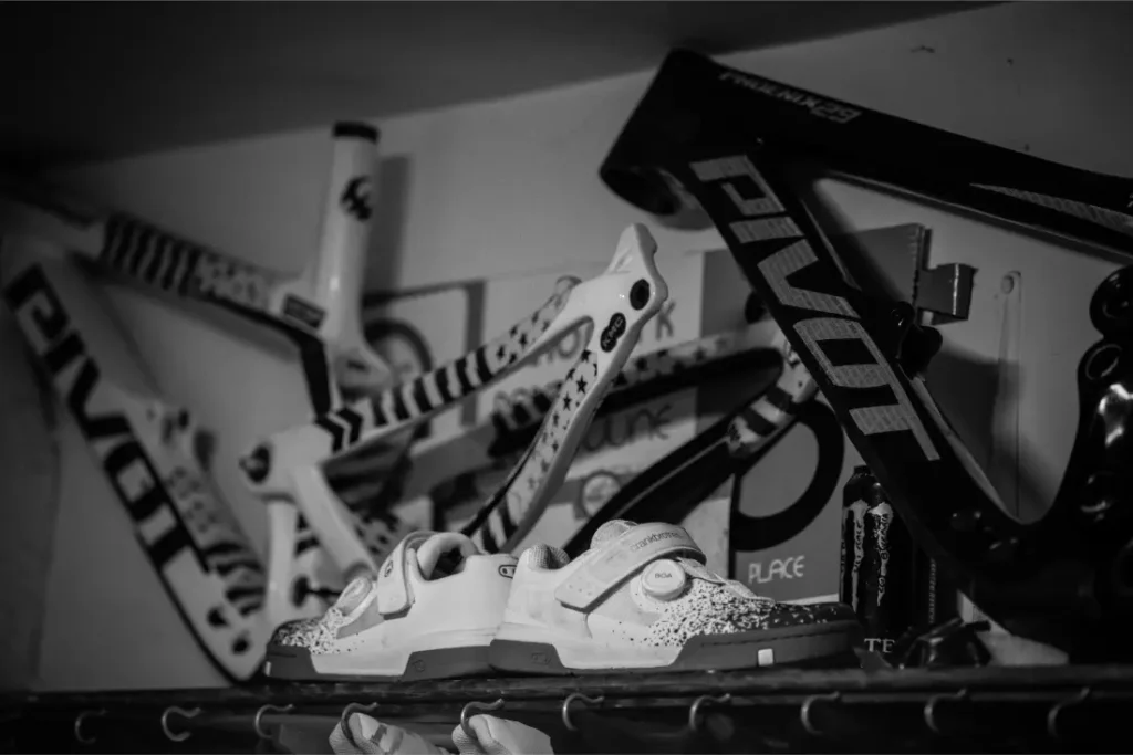 Tres cuadros de bicicleta están montados en una pared encima de una estantería que contiene zapatillas de ciclismo; la imagen en blanco y negro evoca el estilo minimalista admirado a menudo por jordi bagó.