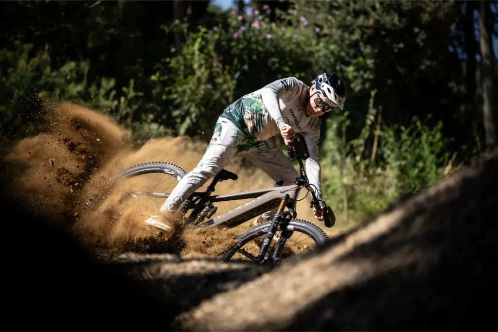 Un ciclista de montaña derrapa en una curva de tierra, levantando polvo, mientras recorre una pista forestal a la luz del día, como los momentos llenos de adrenalina que describe en una entrevista Jordi Bagó.