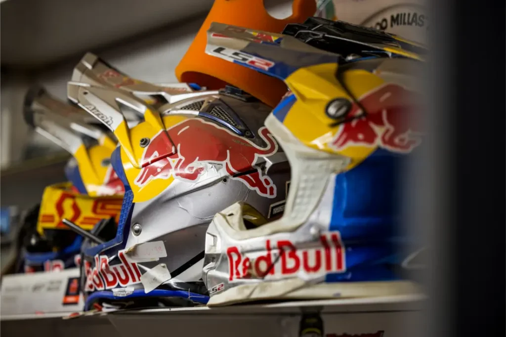 Varios cascos de motocicleta con la marca Red Bull están alineados en un estante, con colores azul, amarillo y plata y destacados logotipos de Red Bull, perfectos para cualquier aficionado después de ver la entrevista a Josep García.