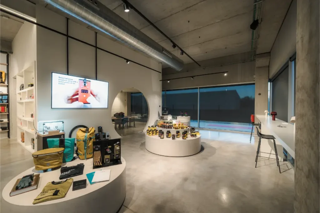 Una moderna tienda de Vic Sports con mesas redondas en las que se exponen aparatos y accesorios, un televisor en la pared, taburetes de bar junto a un mostrador y grandes ventanales por los que entra la luz natural.