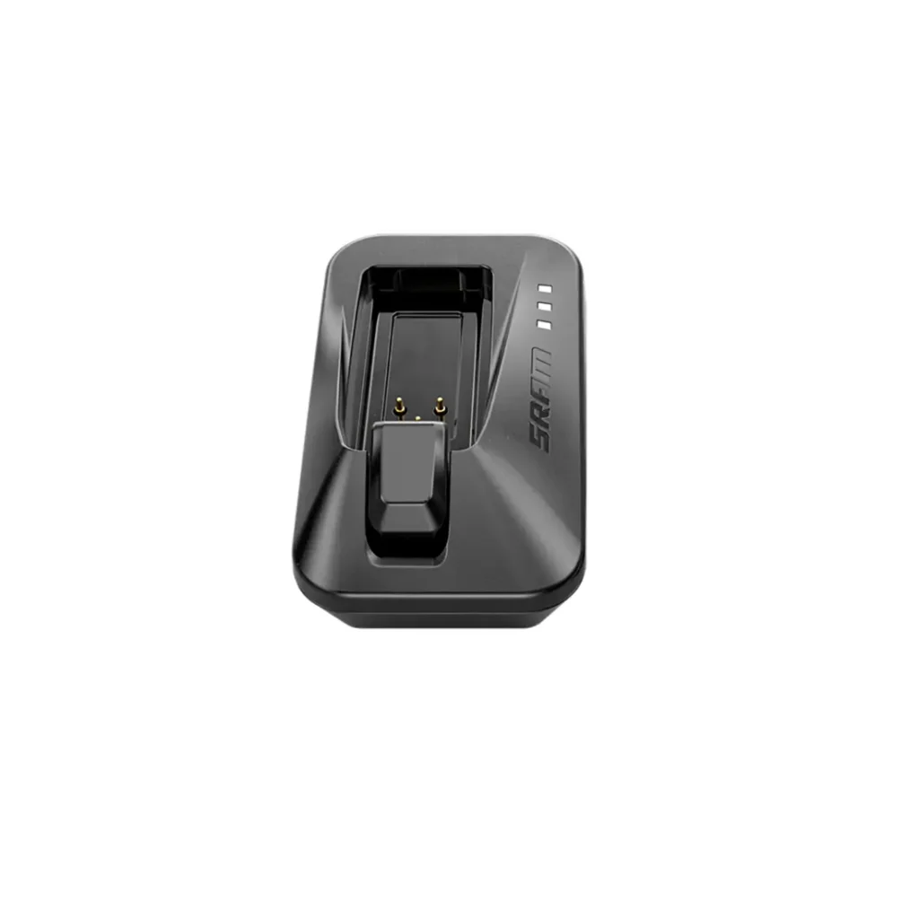 Un cargador de batería SRAM negro con clavijas de carga y luces indicadoras LED sobre un fondo blanco, presentado entre las Novedades SRAM febrero 2026.