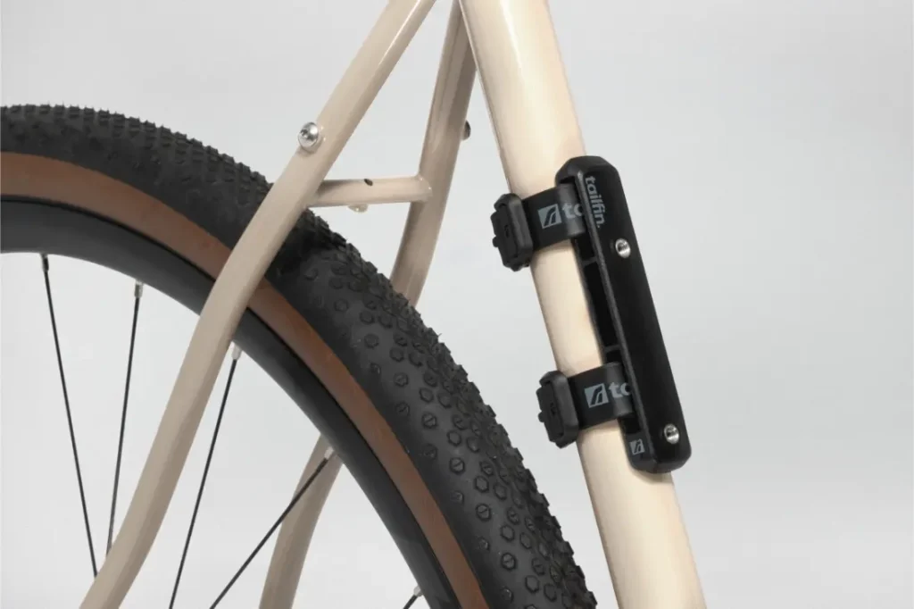 Primer plano de la parte trasera de una bicicleta con cuadro beige, con un accesorio Tailfin Hydromount montado verticalmente cerca de la rueda trasera.