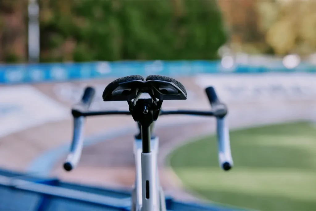 Primer plano de una bicicleta con el sillín y el manillar PRO Stealth 3D, con una pista de velódromo al aire libre difuminada y una exuberante vegetación de fondo.
