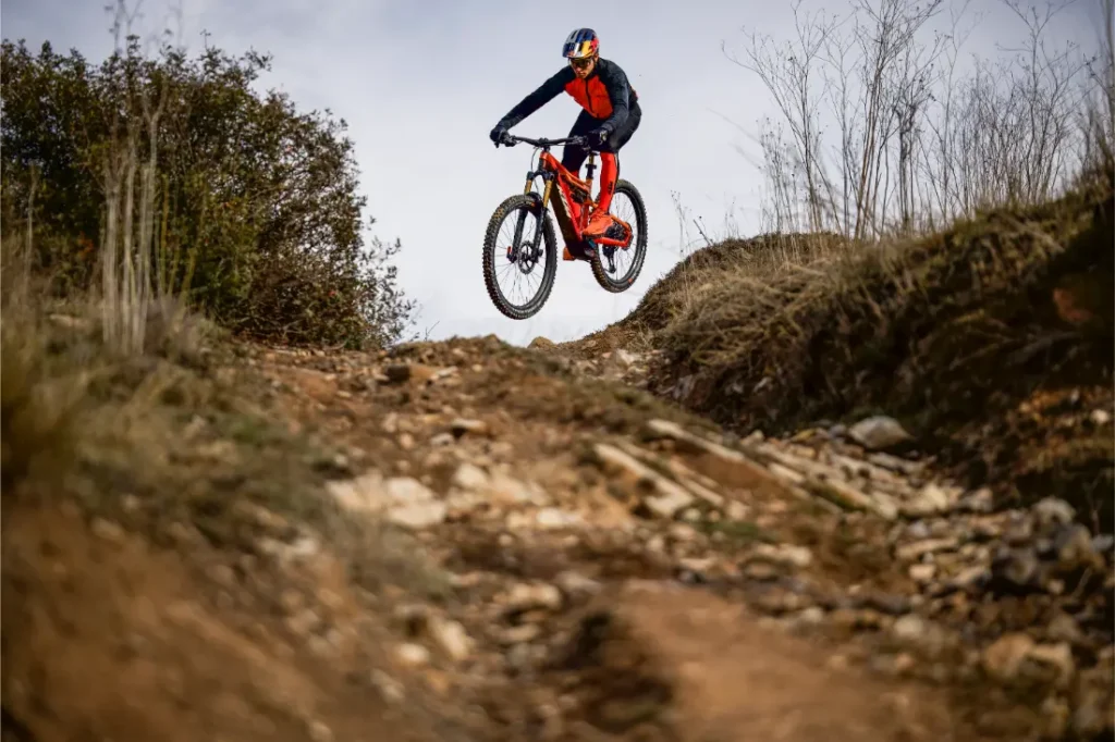 Un ciclista con equipo de protección monta en bicicleta de montaña por un sendero de tierra rocosa y salta por encima de una elevación, como en las escenas descritas en una entrevista a Josep García.