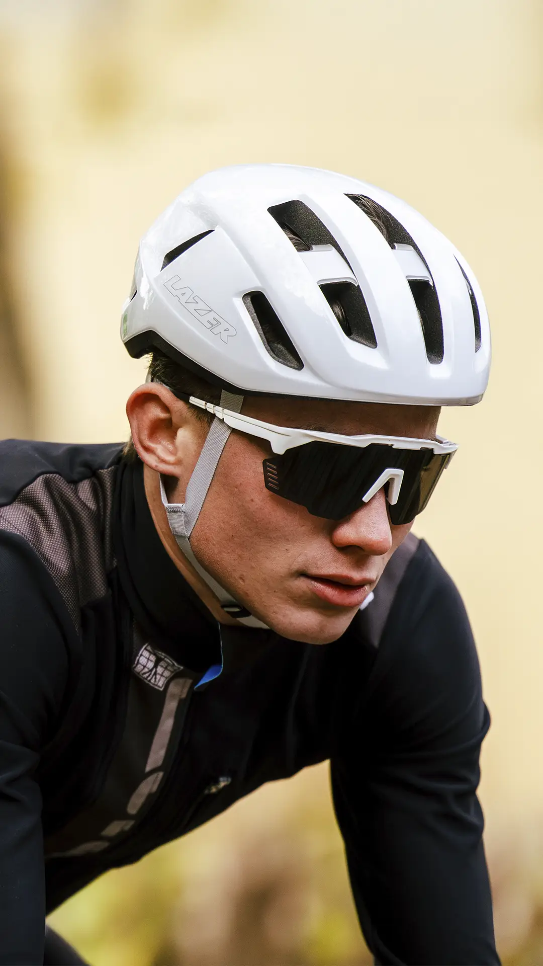 Una persona que lleva un casco de ciclista blanco, gafas de sol negras y un maillot de ciclista negro mira hacia delante mientras monta en bicicleta.