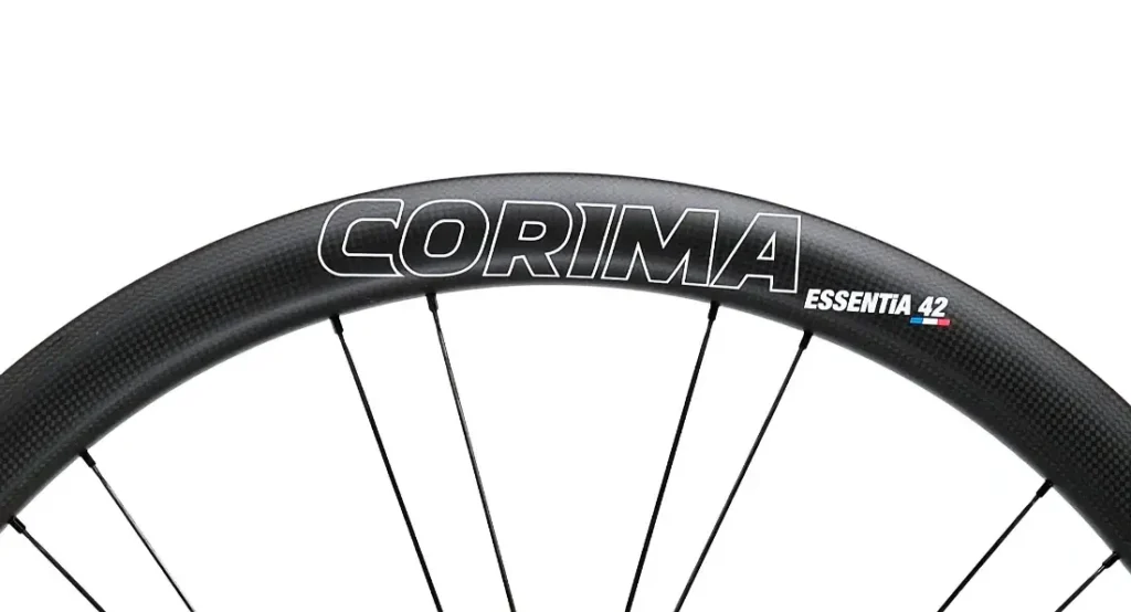 Primer plano de una llanta de bicicleta negra con el nombre de la marca "CORIMA" y el modelo "ESSENTIA 42" impresos, mostrando las Corima Essentia 42 ruedas carretera, ideales para carreras de resistencia.
