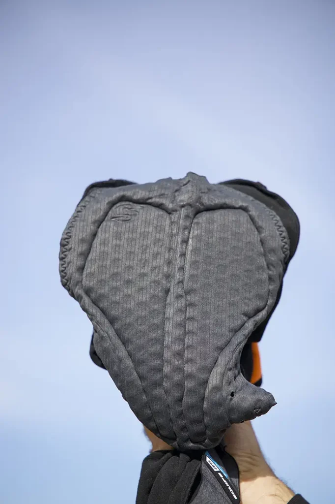 Una mano sostiene un pantalón corto de ciclismo acolchado de color negro contra un cielo azul claro, que recuerda la calidad y la comodidad que se encuentran en la equipación de EQUIPE RS Johdah y chaqueta ASSOS.
