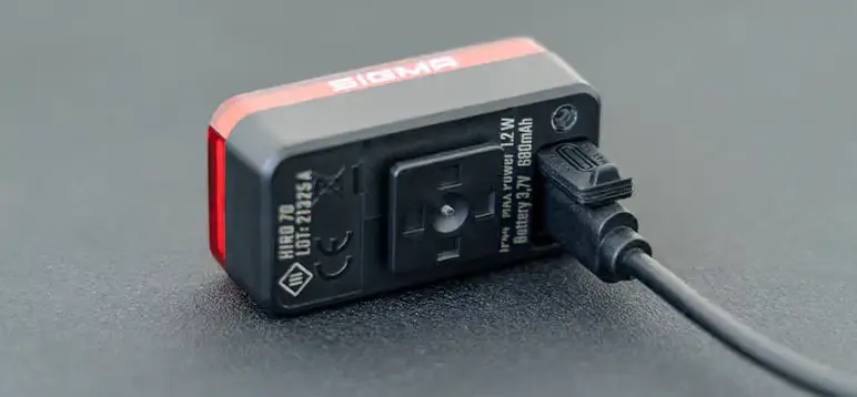Primer plano de un dispositivo Sigma Nyte 70 cargándose a través de un cable USB negro conectado sobre una superficie oscura.
