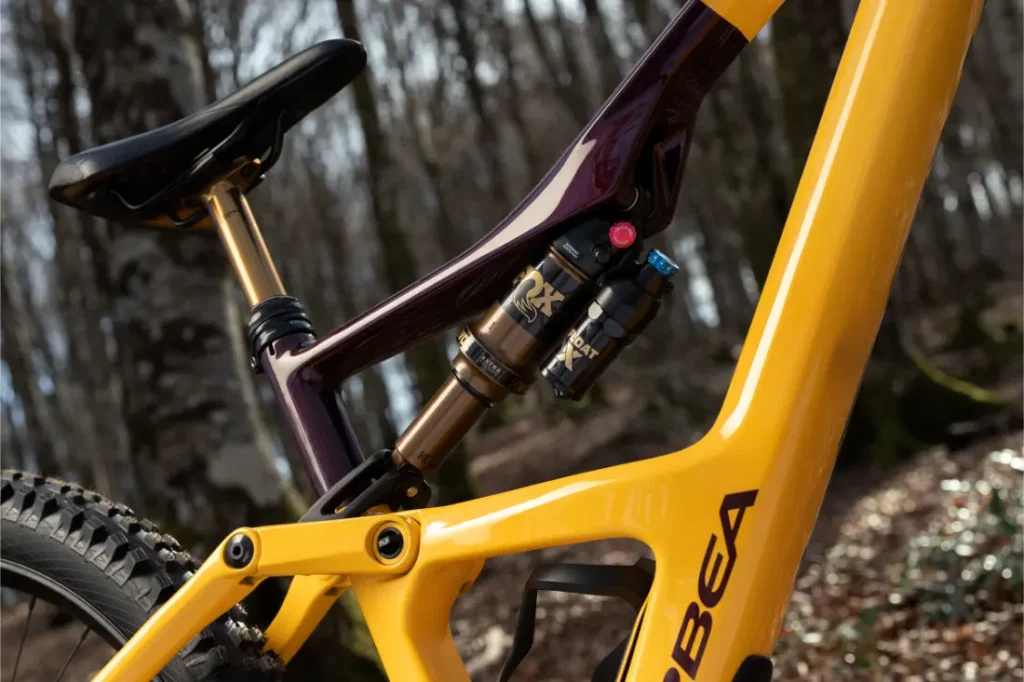 Primer plano de un cuadro de bicicleta de montaña amarillo y morado con amortiguador trasero Fox Float X, que ofrece un ajuste y control precisos. Fotografiada al aire libre en una zona boscosa.