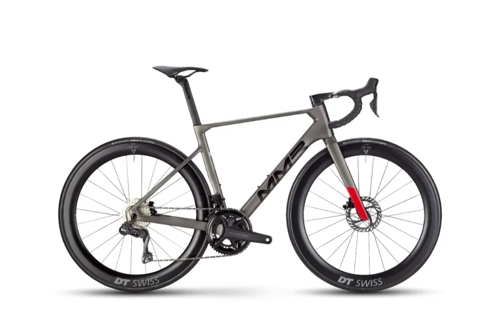 Una moderna bicicleta de carretera, la MMR Aelion SL, cuenta con un cuadro gris mate, ruedas DT Swiss de sección profunda, manillar rebajado y un llamativo acento rojo en la horquilla delantera: pura bici de rendimiento total.