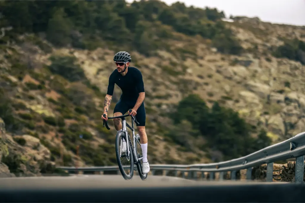 Un ciclista con atuendo negro y casco conduce una MMR Aelion cuesta arriba por una sinuosa carretera de montaña con guardarraíles y árboles de fondo, mostrando el verdadero espíritu bici total.