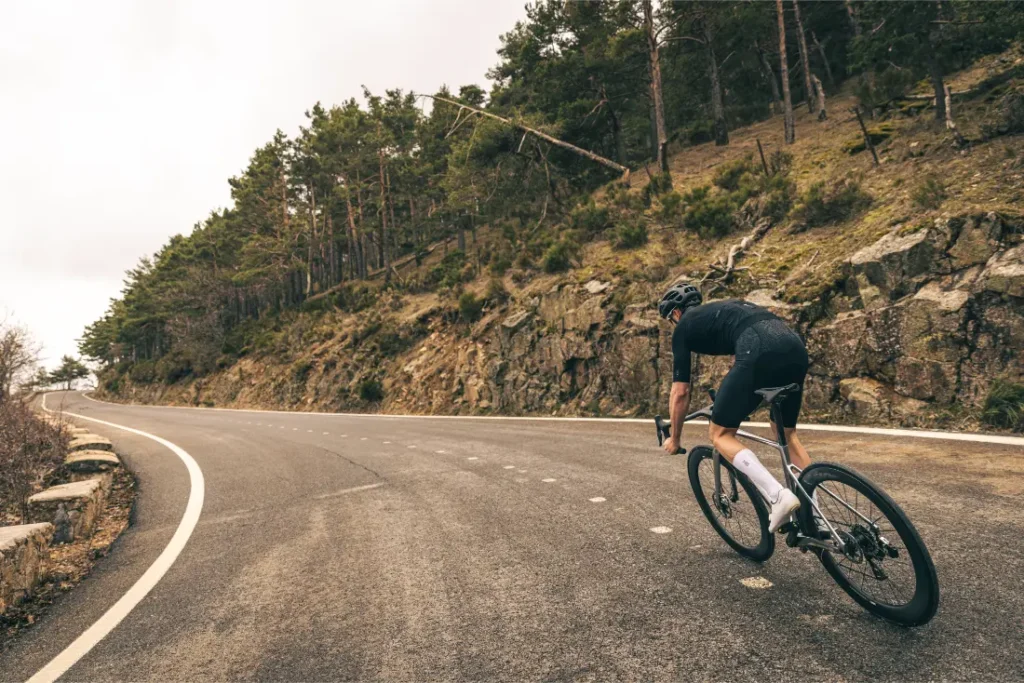 Un ciclista vestido de negro conduce un MMR Aelion cuesta arriba por una carretera sinuosa y vacía bordeada de árboles y terreno rocoso.