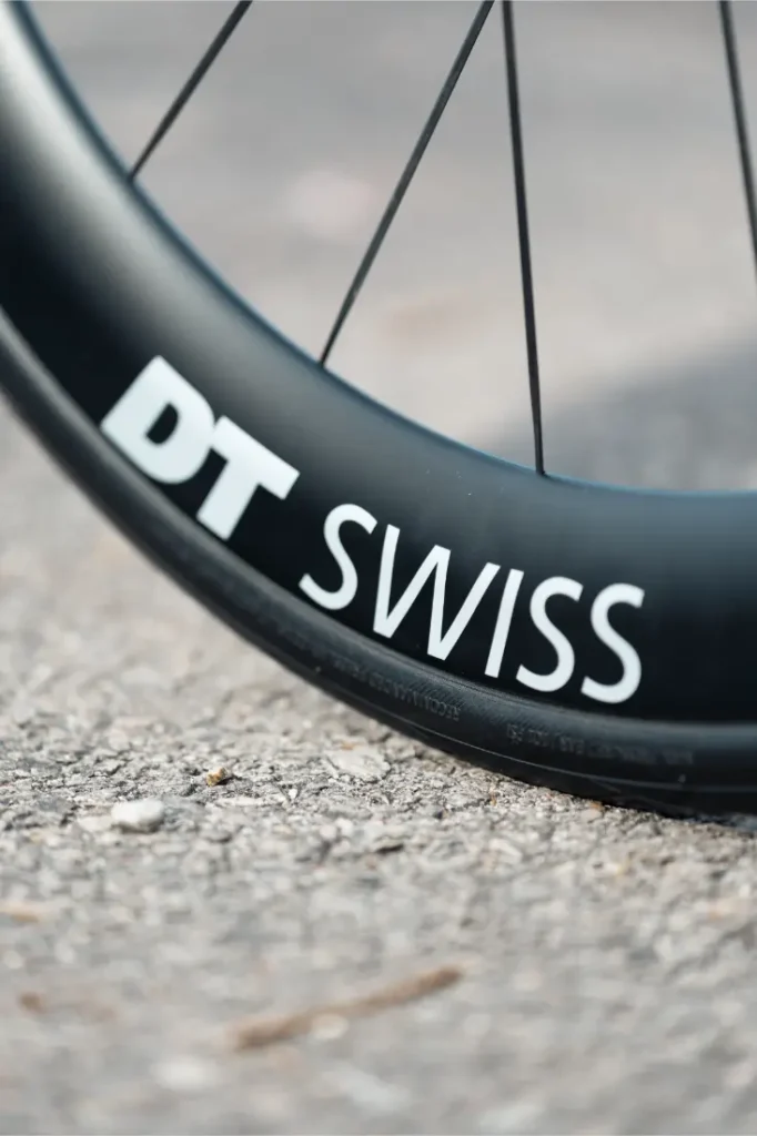 Primer plano de una llanta de bicicleta con la marca "DT SWISS", colocada sobre una superficie de pavimento con textura, perfecta para mejorar su MMR Aelion o cualquier actualización total de bicicleta.