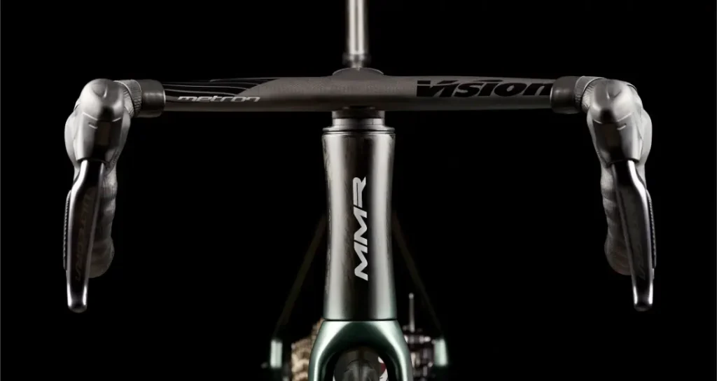 Vista frontal en primer plano del manillar, las manetas de freno y el tubo de dirección de una MMR Aelion SL sobre un fondo negro: una auténtica bici total.