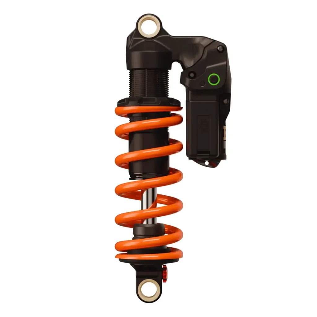 Primer plano de un amortiguador negro y naranja de bicicleta o motocicleta, con un componente electrónico acoplado, que muestra ingeniería con el factor X.