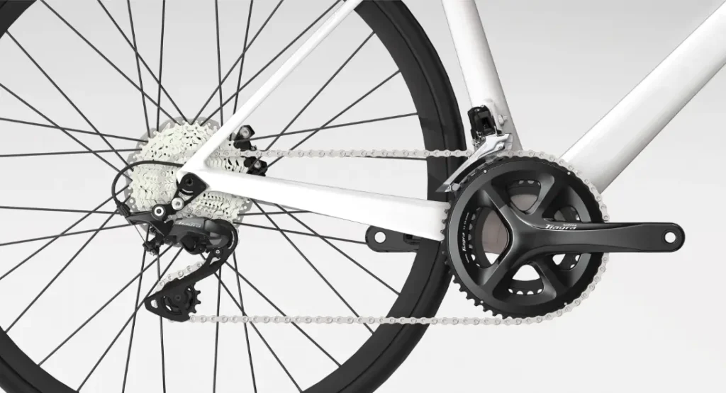 Primer plano de una transmisión de bicicleta con el cambio trasero Shimano Tiagra R4000, el casete, la cadena y las bielas sobre un fondo blanco.
