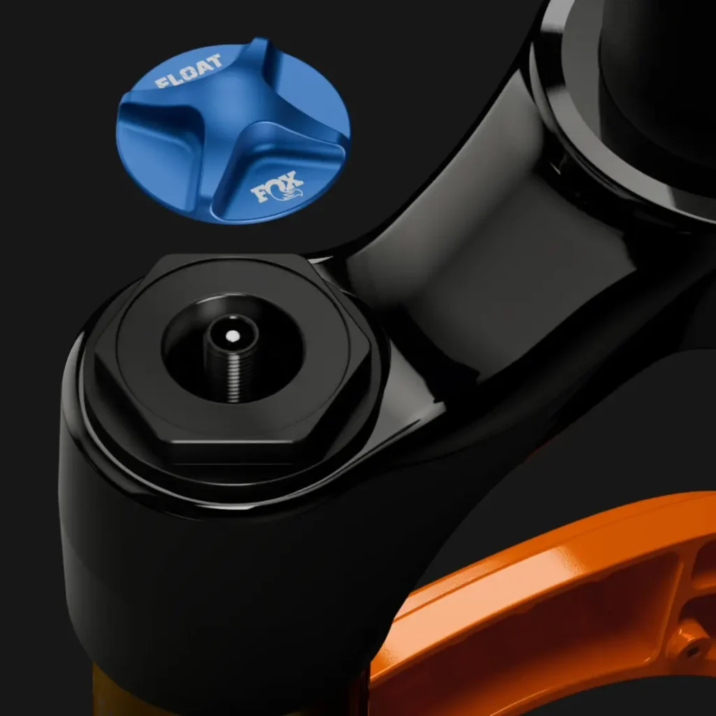 Primer plano de una horquilla de suspensión FOX 38 2027 Enduro que muestra un mando de ajuste FOX Float azul, destacando el control preciso y los elegantes componentes negros y naranjas sobre un fondo oscuro.