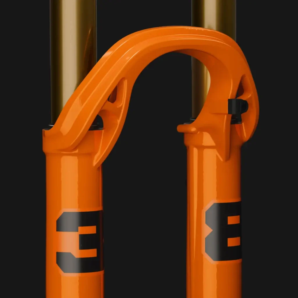 Primer plano de una horquilla de suspensión FOX 38 2027 de color naranja para una bicicleta, con números negros y dos tubos de montante dorados, diseñada para la práctica del Enduro, sobre un elegante fondo negro.