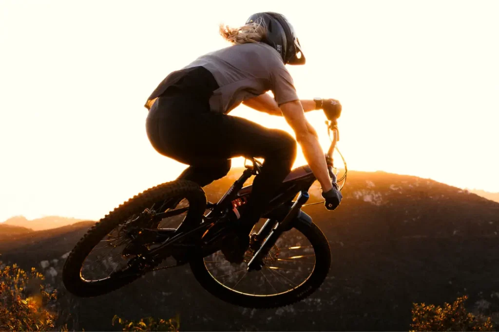 Una persona con casco conduce una bicicleta de montaña con horquillas FOX 38 2027 fuera de la carretera al atardecer, mostrando el control del enduro mientras recorren colinas bajo un cielo brillante.