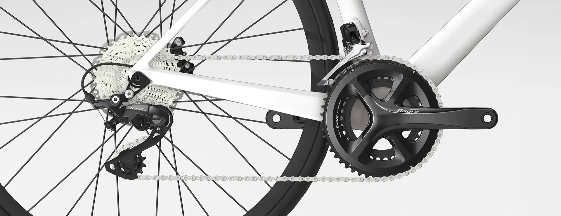 Primer plano de la transmisión de una bicicleta, con el cambio trasero, el casete, la cadena y las bielas Shimano Tiagra R4000 en un elegante cuadro blanco.
