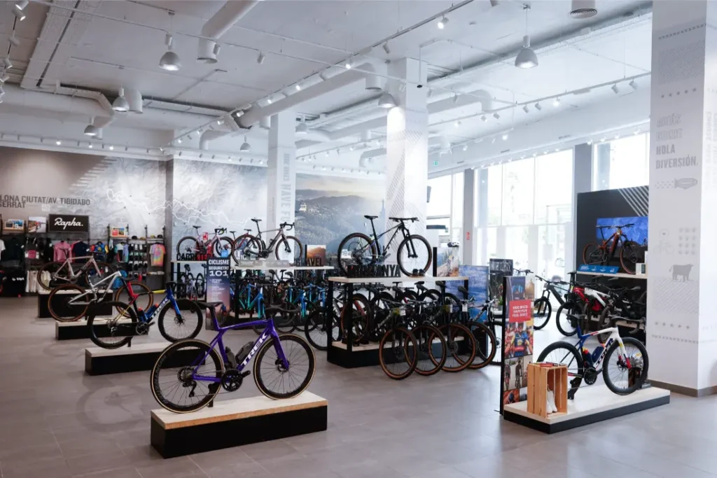 Una tienda de bicicletas espaciosa y bien iluminada que muestra varias bicicletas en stands y bastidores, incluidos los modelos Trek BCN Sud, con accesorios de ciclismo y equipos a lo largo de las paredes como socio oficial de Gravel Penedès.