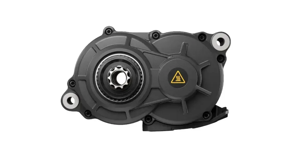 Primer plano de una carcasa de engranaje mecánico Avinox M2S negra con un engranaje metálico central y un símbolo de advertencia amarillo en el lado derecho, aislado sobre fondo blanco.