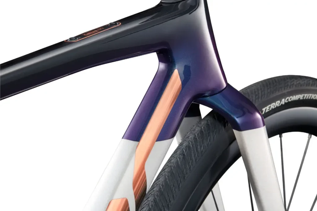 Primer plano de un cuadro de bicicleta BMC Kaius 01 con un diseño elegante con detalles en azul metálico y cobre, y un neumático trasero visible con la marca "TERRACOMPETITION": una bicicleta rápida y capaz.
