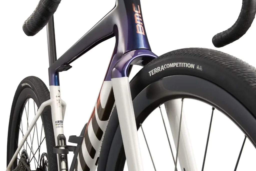Primer plano de la rueda delantera, la horquilla y el cuadro de la BMC Kaius 01 bicicleta rápida, destacando el neumático Terra Competition y los elementos de diseño aerodinámico.