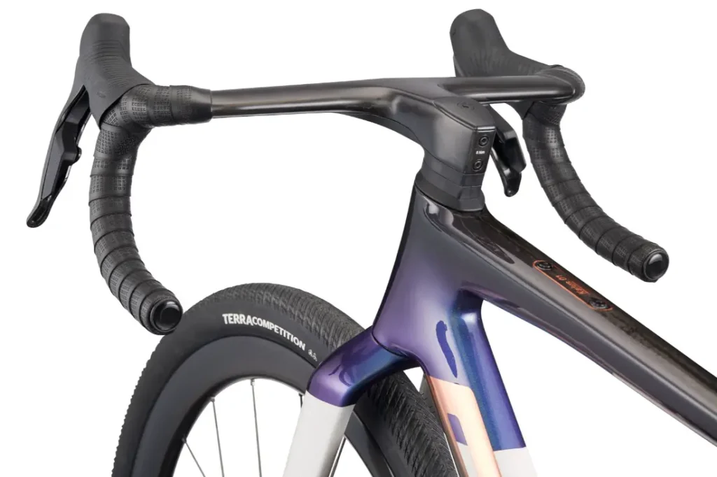 Primer plano del manillar, la potencia y la rueda delantera de una bicicleta de carretera BMC Kaius 01, con puños envolventes y cuadro brillante con acabado de pintura degradada: una bicicleta rápida y capaz en cada detalle.