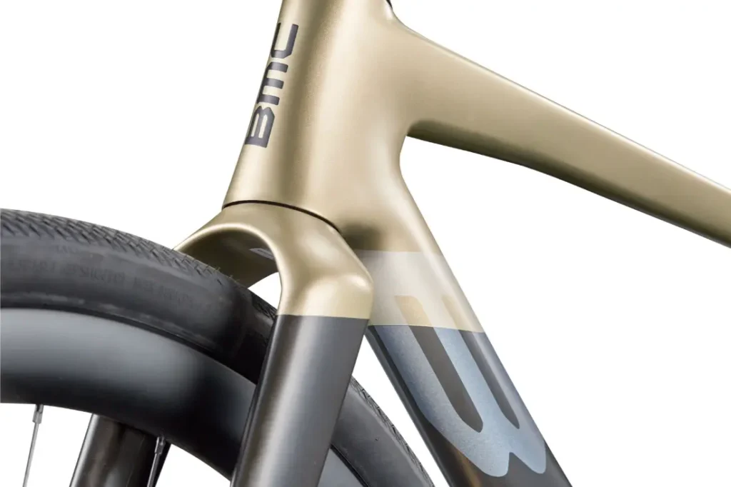 Primer plano de la horquilla delantera y el cuadro de una bicicleta rápida, en el que se aprecia el logotipo de BMC y parte de la rueda delantera, destacando el elegante diseño de la BMC Kaius 01, una bicicleta actual sobresaliente.