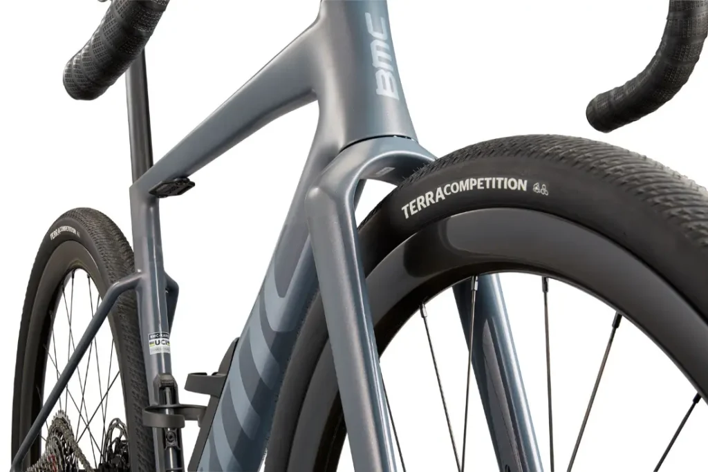 Primer plano de una BMC Kaius 01 centrado en la horquilla delantera, la rueda y la cubierta TERRA COMPETITION con un cuadro gris mate: una bicicleta rápida diseñada para ofrecer el máximo rendimiento.
