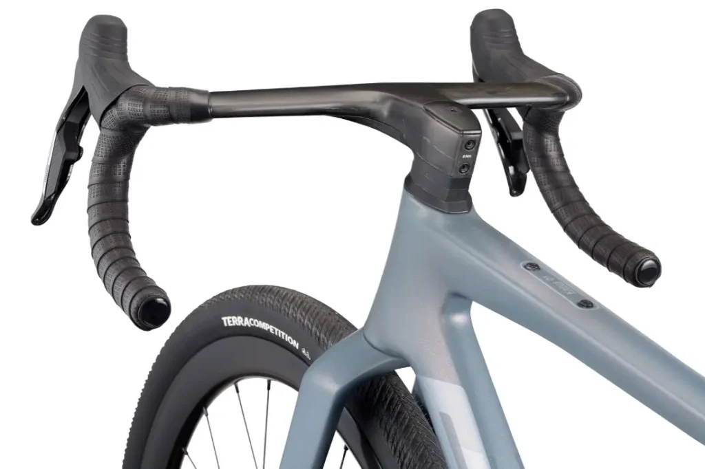 Primer plano de la parte delantera de una BMC Kaius 01, que muestra un manillar rebajado con manetas de freno integradas y un neumático delantero ancho con la etiqueta "Terra Competition", una bicicleta rápida y capaz de realizar recorridos exigentes.