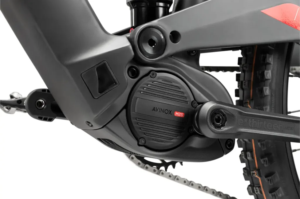 Primer plano de un motor de bicicleta eléctrica Rotwild R.EXC con la etiqueta "AVINOX M25" montado cerca de la biela, con la cadena, el pedal y parte de la rueda trasera visibles, fabricado para competir al más alto nivel.