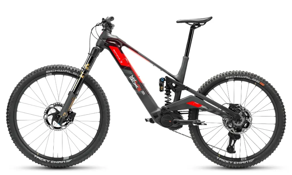Bicicleta eléctrica de montaña Rotwild R.EXC con suspensión total, neumáticos de tacos gruesos, frenos de disco y cuadro negro y rojo, diseñada para competir en senderos difíciles, mostrada de perfil sobre fondo blanco.