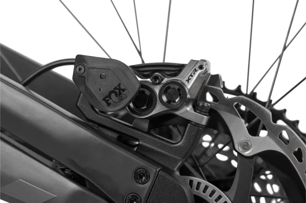 Primer plano de la pinza y el rotor del freno de disco trasero de una bicicleta de montaña Rotwild R.EXC, que muestra componentes detallados y parte del cuadro en tonos negros y plateados, diseñado con precisión para los amantes de la competición.